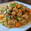Nouilles sautées au poulet caramélisé dans une assiette garnie de légumes frais.